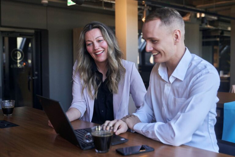 Två personer sitter framför en dator med glada ansiktsuttryck och arbetar med onboarding