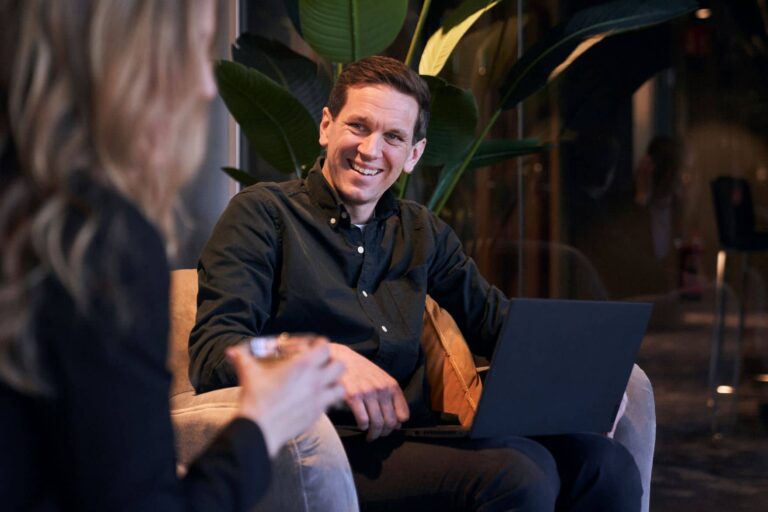 En man sitter i samtal med en kvinna med en laptop i knät och berättar om AI i rekytering