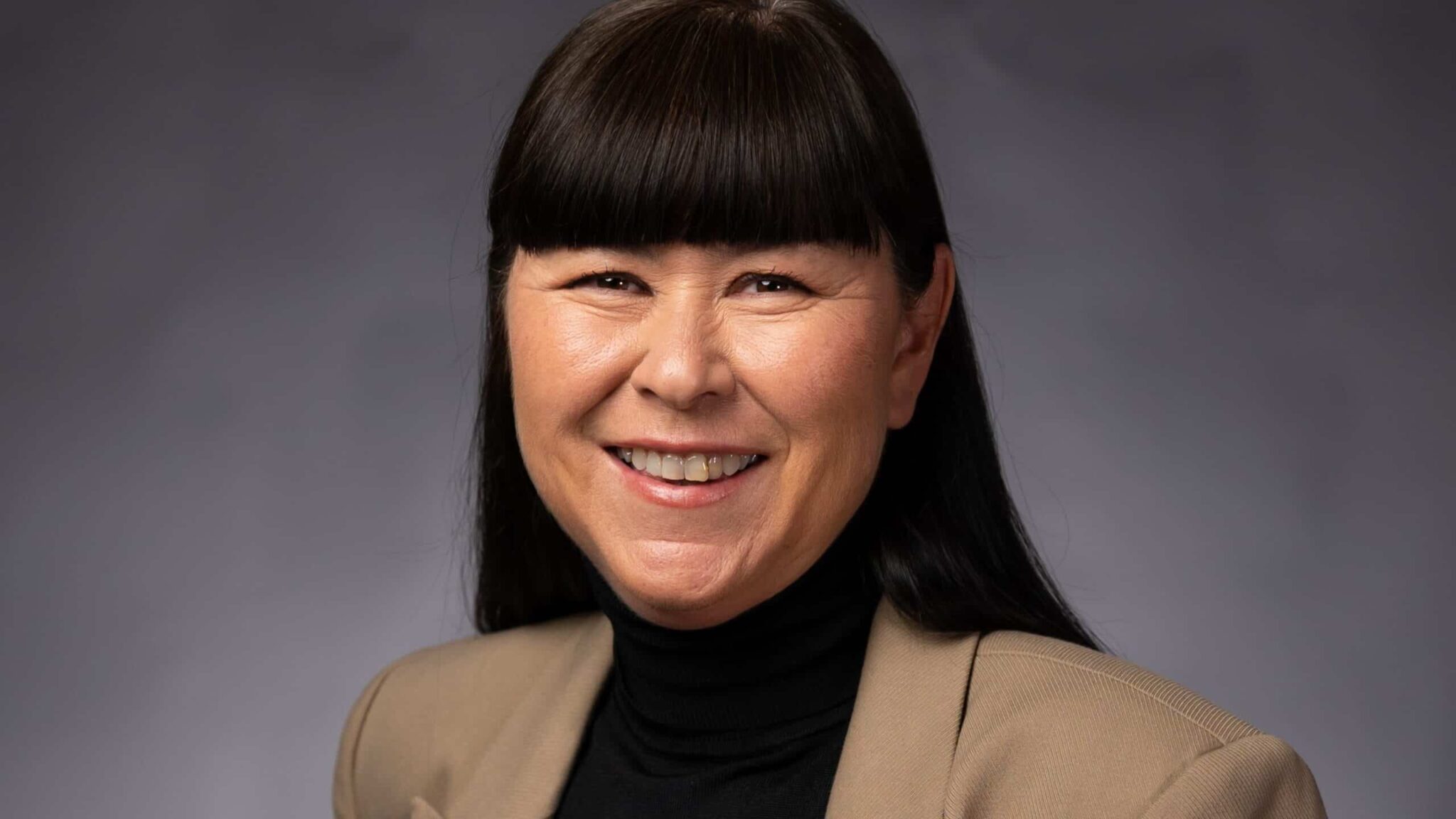 Katarina har svart hår och lugg och en beige kappa och ler och arbetar med HR